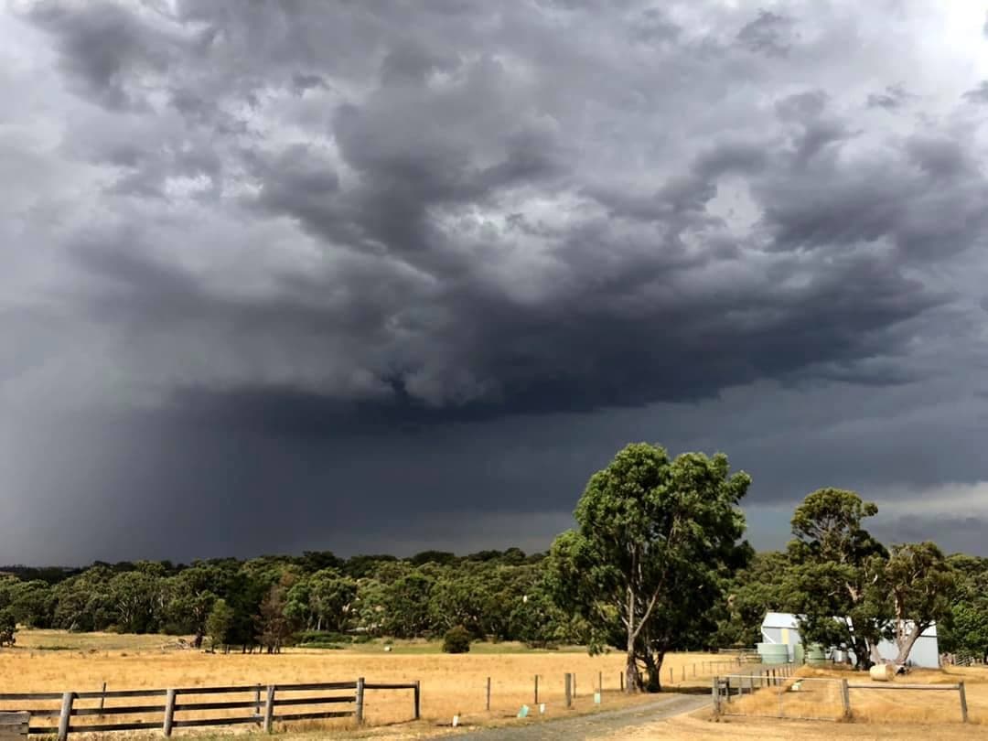 A towering storm front rolling in over the dry summer paddocks and hay shed